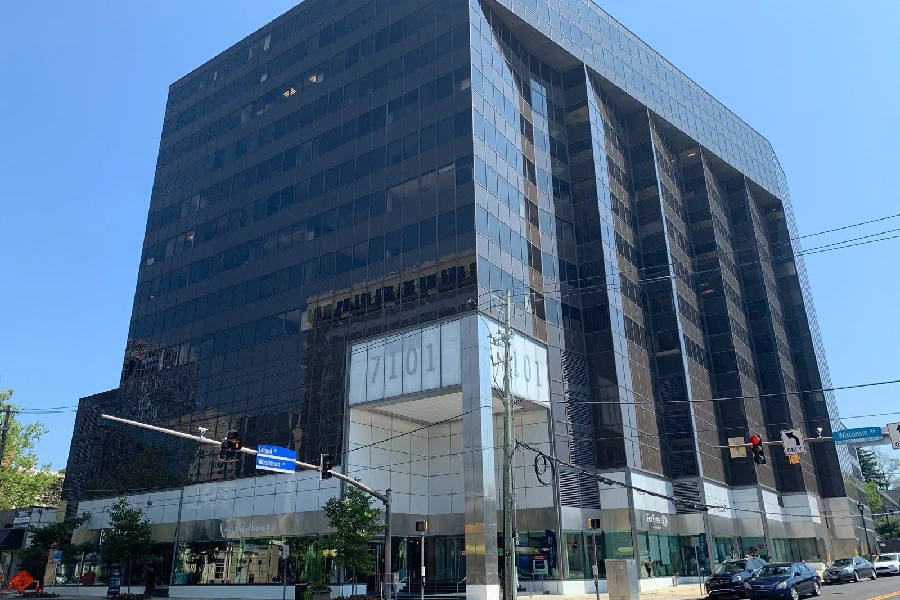 A large, modern glass office building with dark reflective windows, located on a city street corner under a clear blue sky.